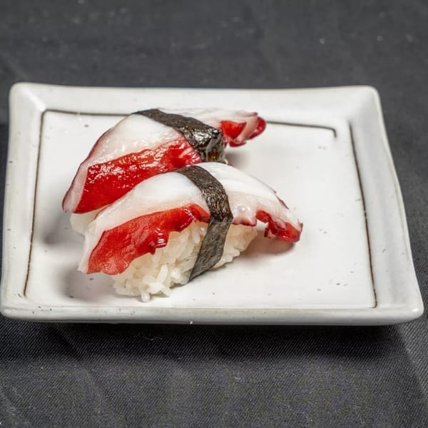 Two pieces of octopus nigiri sushi with red and white tentacles on a white rectangular plate.