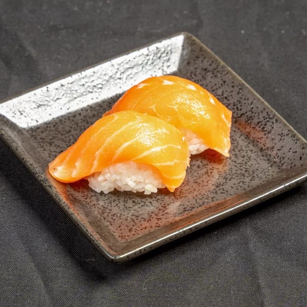 Two pieces of salmon nigiri sushi with bright orange fish on white rice, served on a dark textured plate.