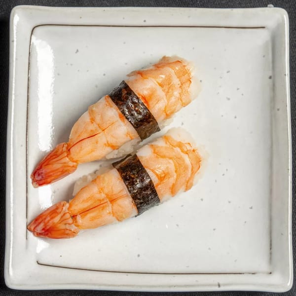 Two pieces of shrimp nigiri sushi, with bright orange shrimp and dark nori, on a white square plate.