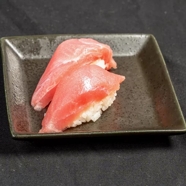 Two pieces of fresh tuna nigiri sushi with white rice on a dark rectangular plate.