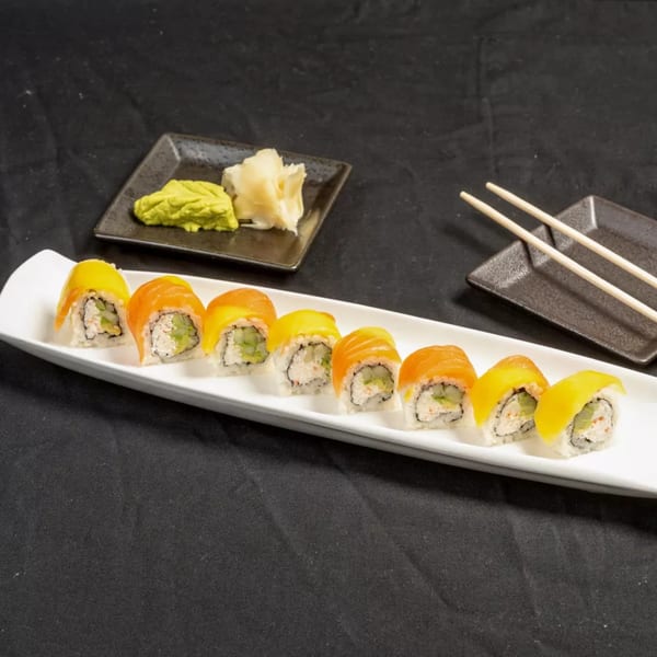 Sushi rolls with salmon and mango on a white plate, with wasabi, ginger, and chopsticks.