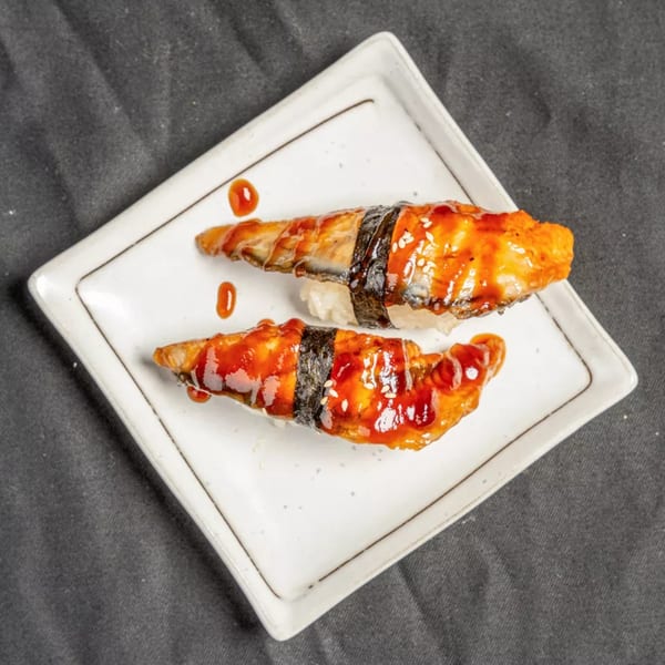 Two pieces of unagi nigiri sushi with sweet sauce and sesame seeds on a white plate.