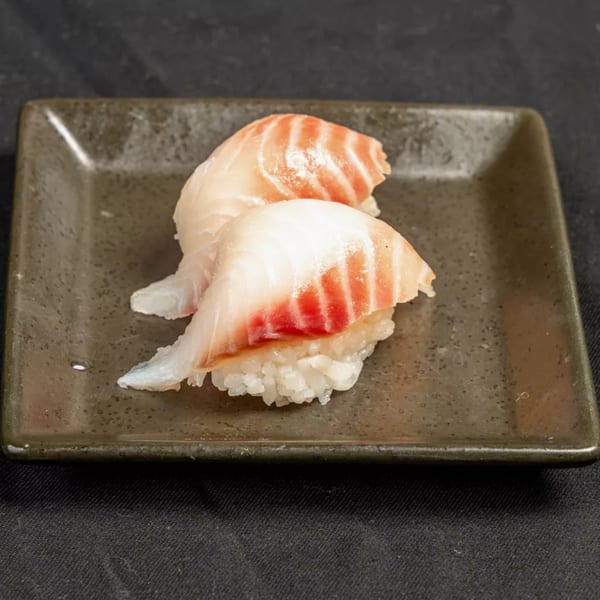 Two pieces of nigiri sushi with white fish and red stripes on a dark rectangular plate.